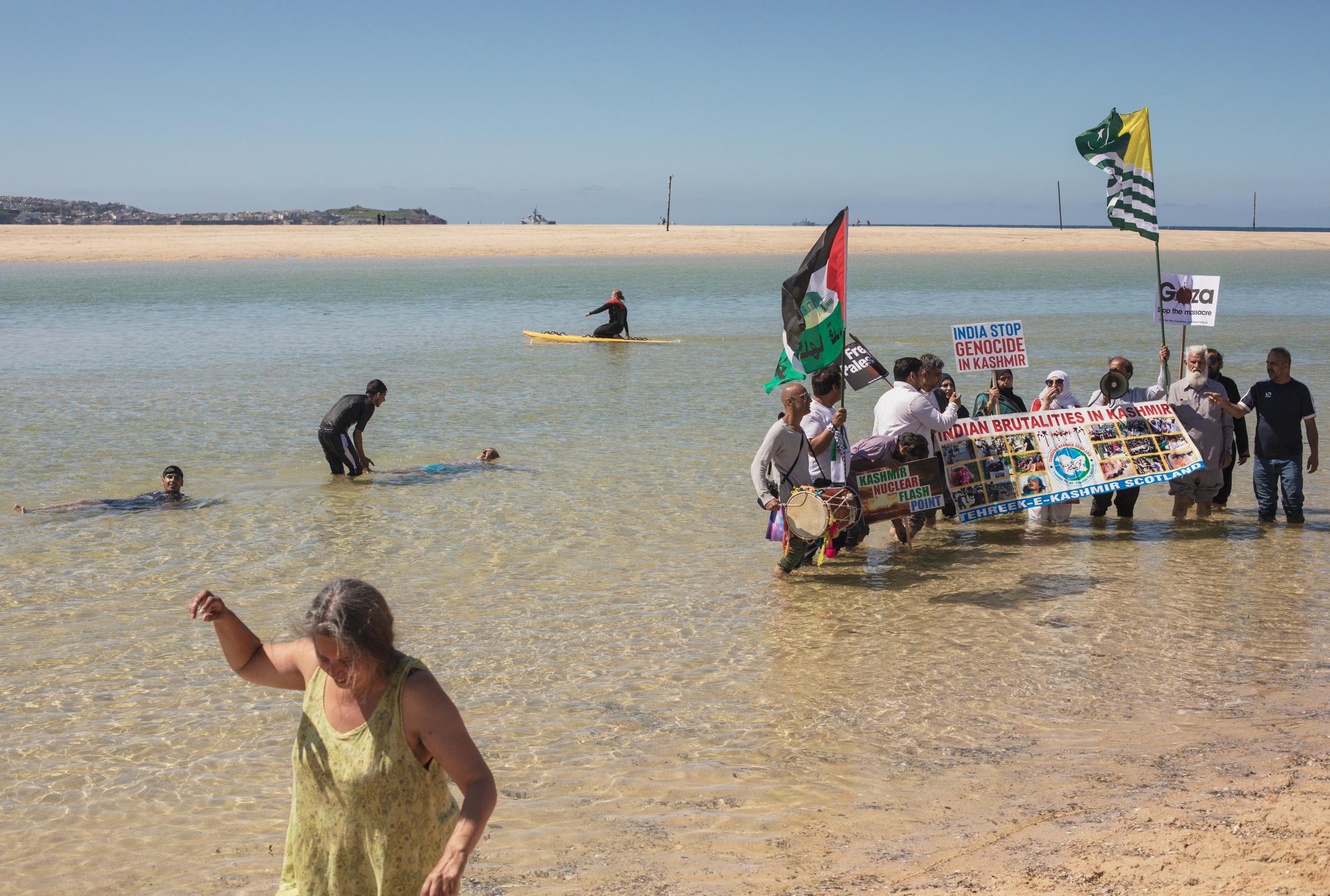 A group of protesters gather in the water as other play in the water.