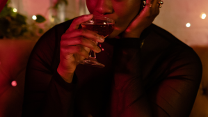 A non-binary person sipping a drink at a bar.