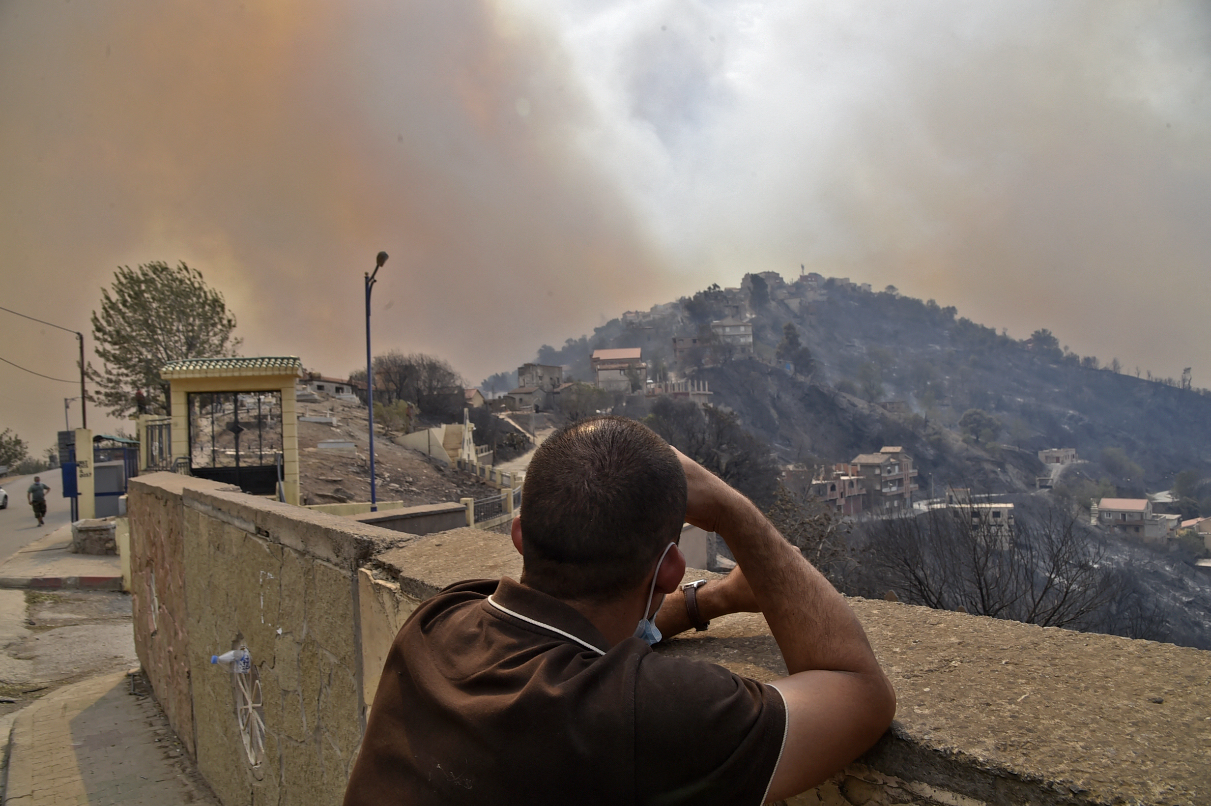 A man looks on as smoke rises from a wildfire in the forested hills. Photo: RYAD KRAMDI/AFP via Getty Images