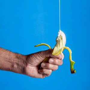Eine Banane in einer Hand wird mit weißer Soße übergossen, hier sind Ratschläge für einen unvergesslichen Handjob.