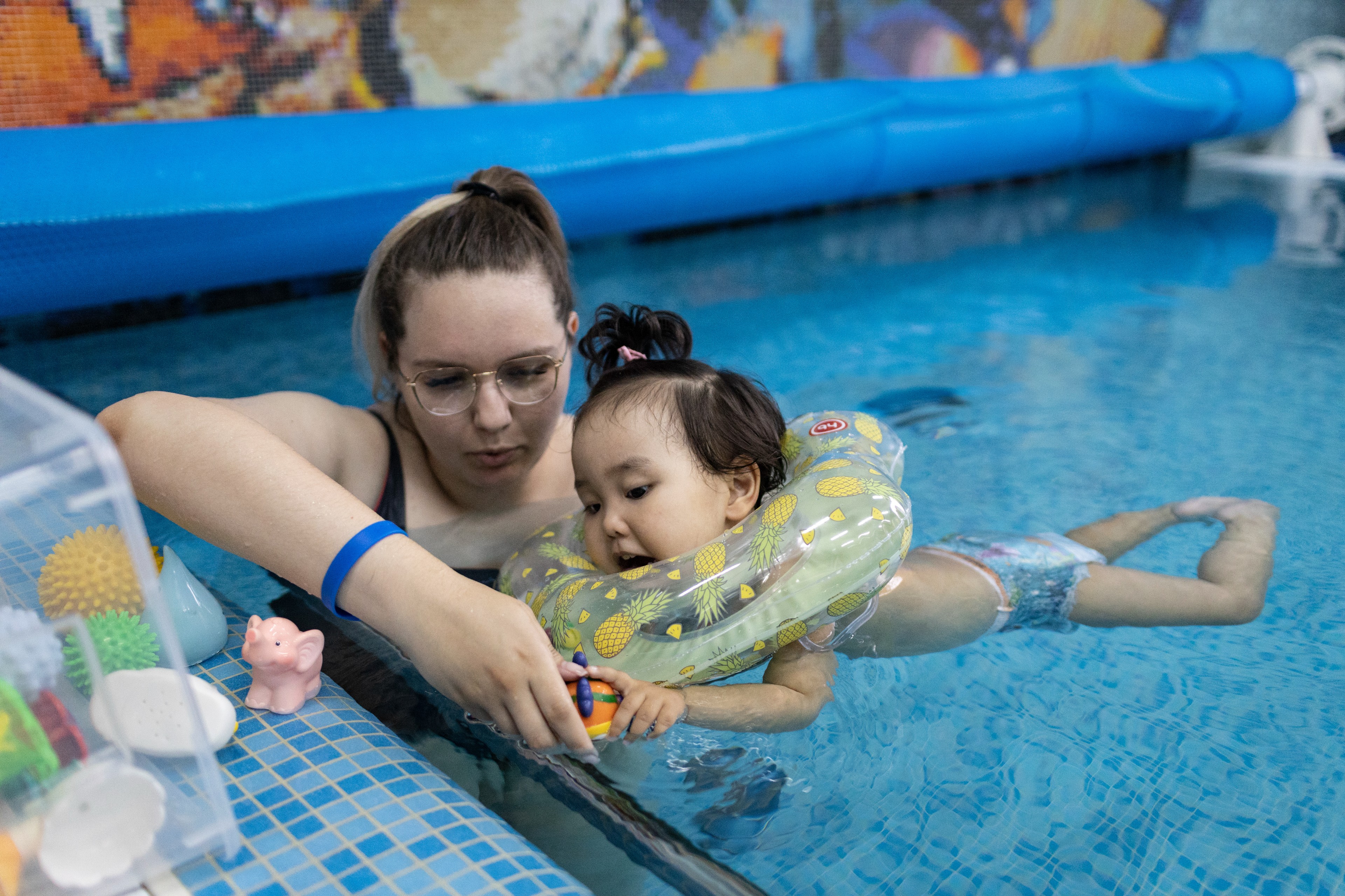 Eine junge Frau spielt mit einem Kleinkind mit Schwimmreifen in einem Schwimmbecken
