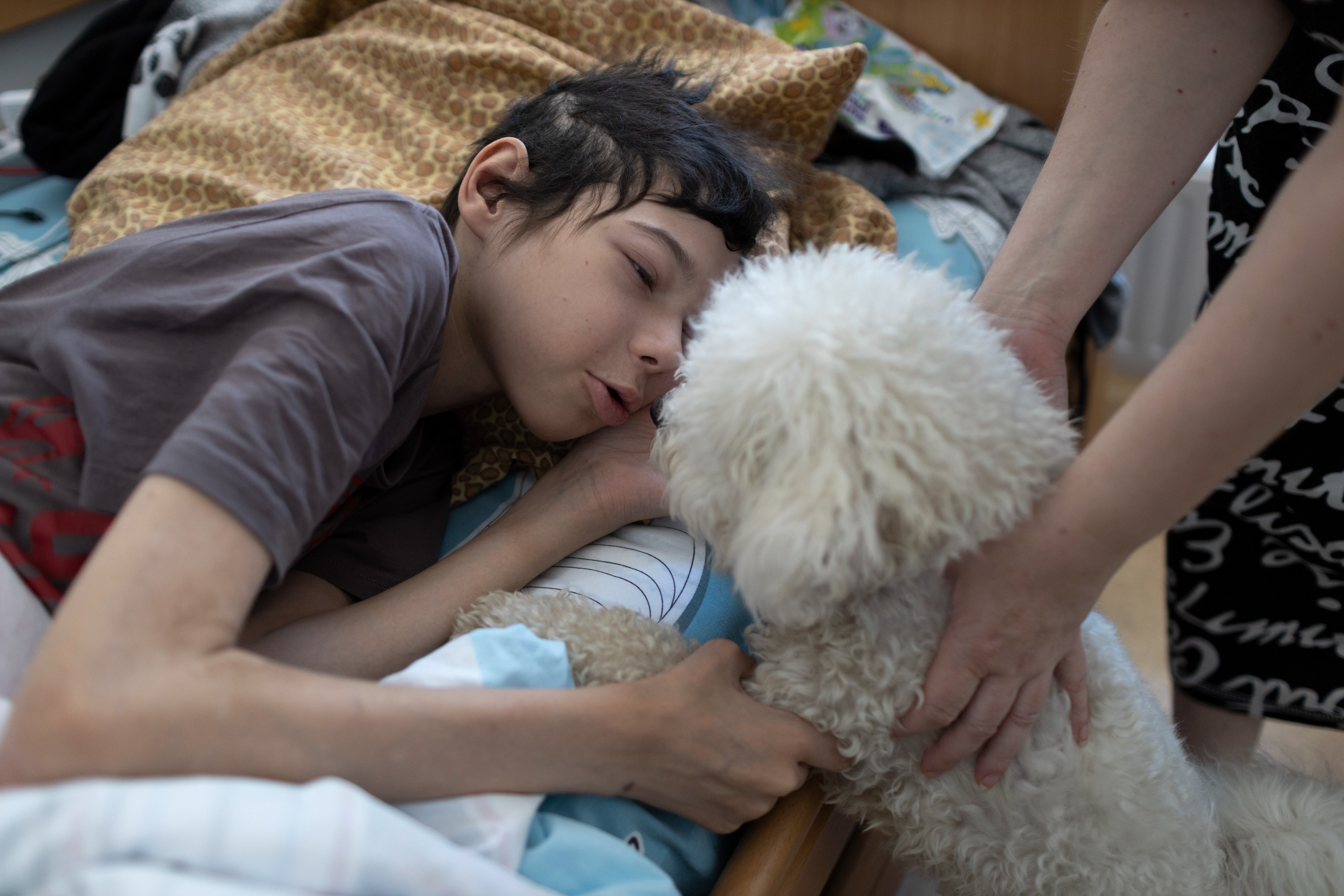 Ein dünner Junge spricht mit einem kleinen weißen Hund, der mit den Vorderbeinen auf seinem Bett ist