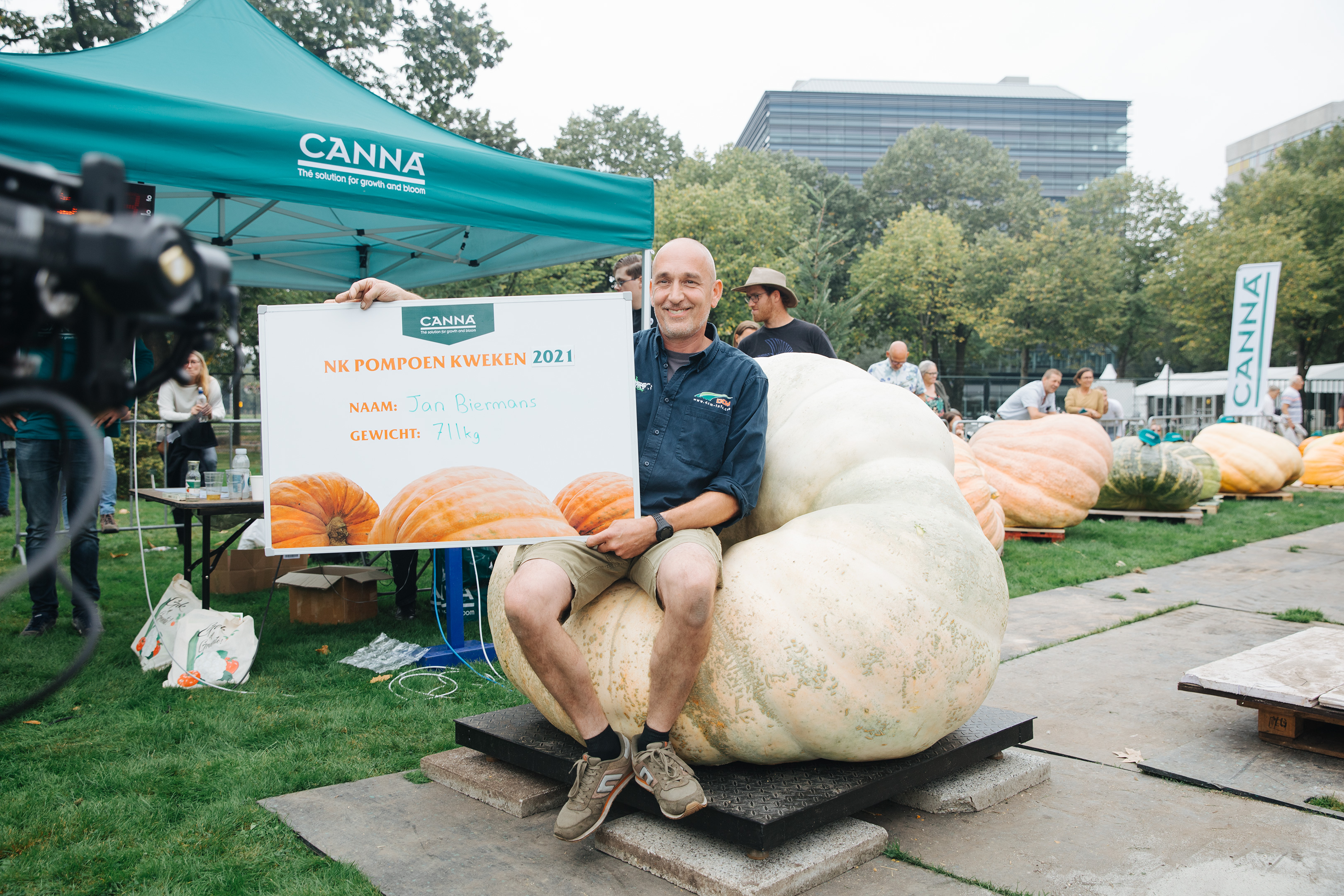 Raymond van Mil, Netherlands, pumpkins - Bald man in shorts sat on a giant pumpkin holding up a large certificate to the camera.