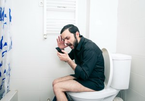 A man sitting on the toilet, yelling at a smartphone.