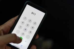 Hand holding cell phone with emergency number 911 on black background​
