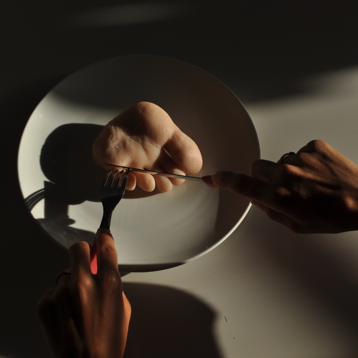 Matteo Ingrao, sculpture, art - Photo of a sculpted human foot on a white plate, disembodied hands carving it with a knife and fork.