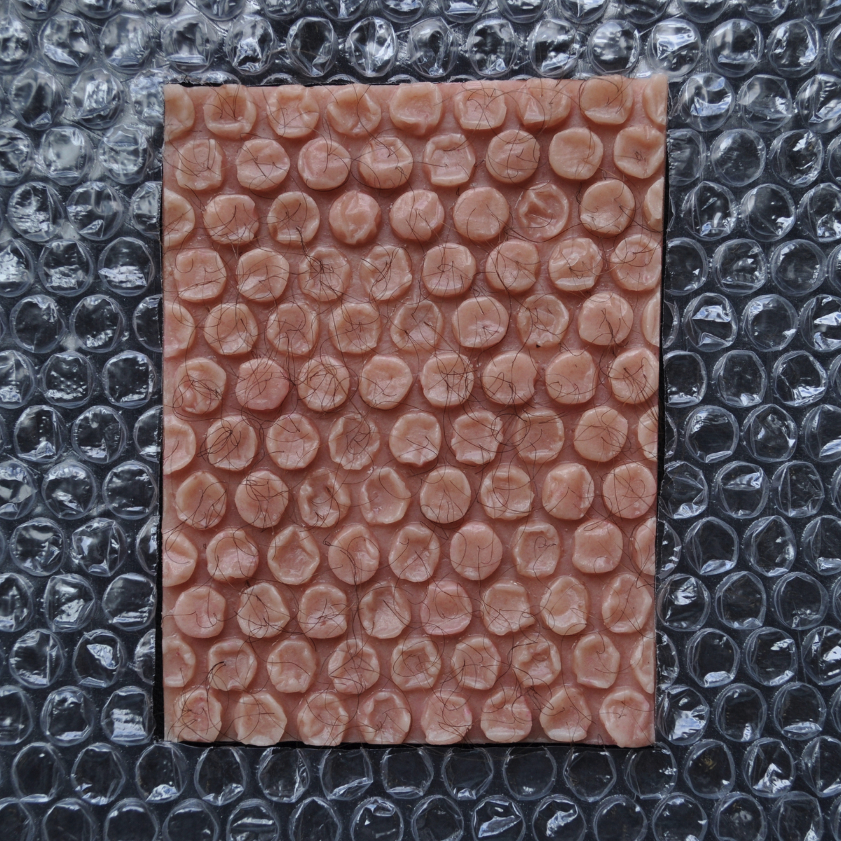 Matteo Ingrao, sculpture, art - Sculptural work, a square of human flesh resembling bubble wrap laid on top of a sheet of bubble wrap.
