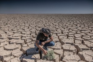 Climate change, Iraq - Photograph of a man wearing blue jeans crouched down in a cracked, parched river basin.