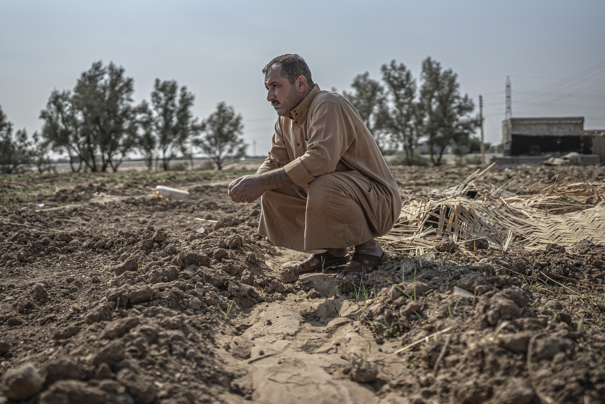 Climate crisis, Iraq - Photograph of a man in traditional dress kneeling in dried mud.