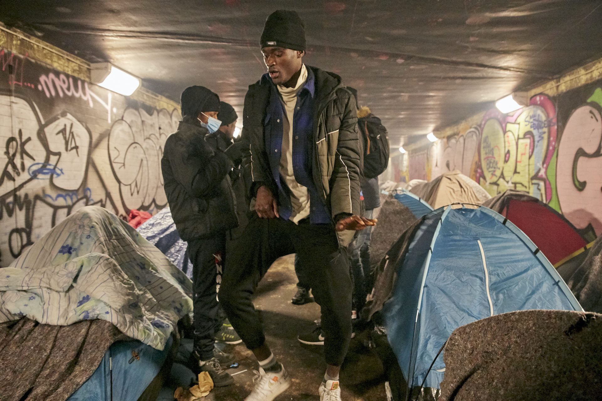 Paris refugees Porte Brunet – four teens standing inside of the tunnel in between tents and dancing.