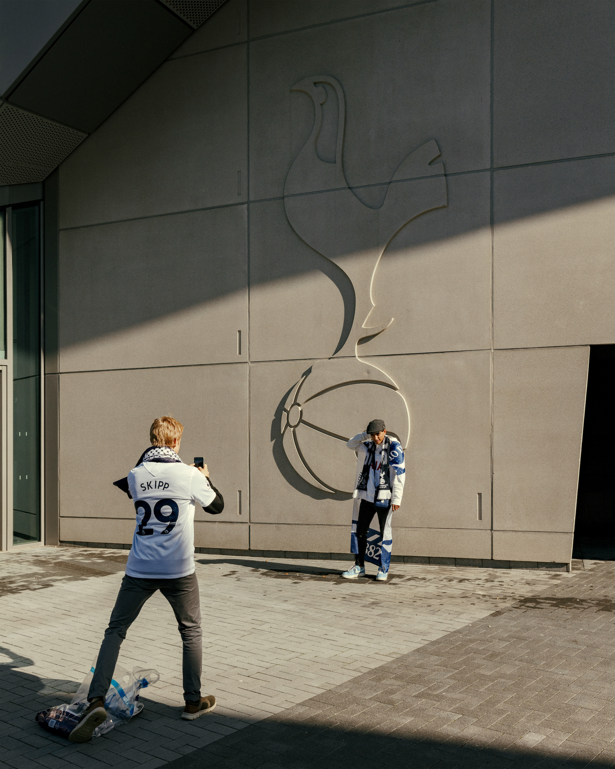 A fan poses in front of a giant Spurs logo imprinted on the side of the stadium