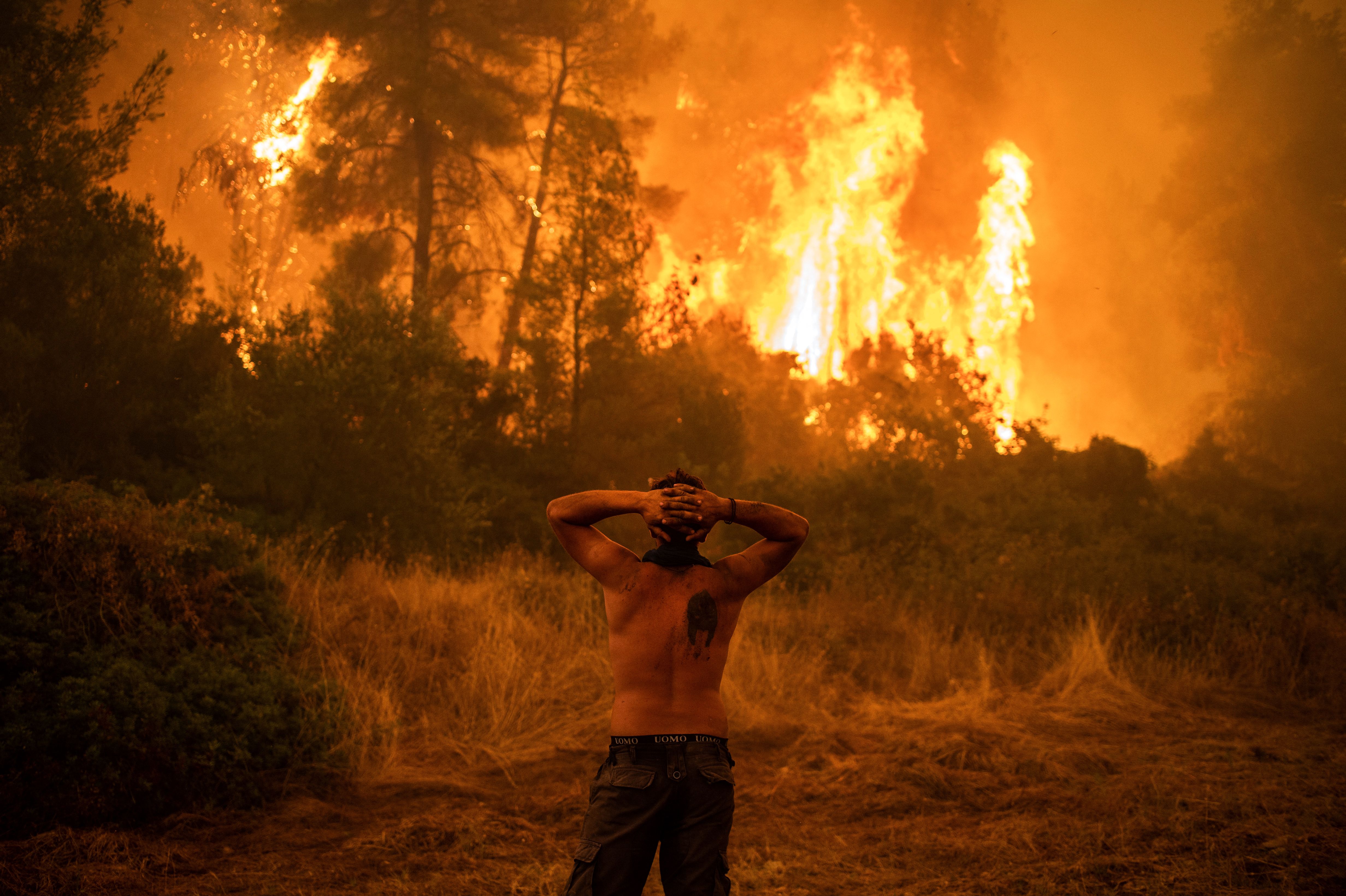 Un uomo guarda un incendio che si avvicina a Pefki, nell'isola greca di Evia, ad agosto. Foto: ANGELOS TZORTZINIS/AFP via Getty Images