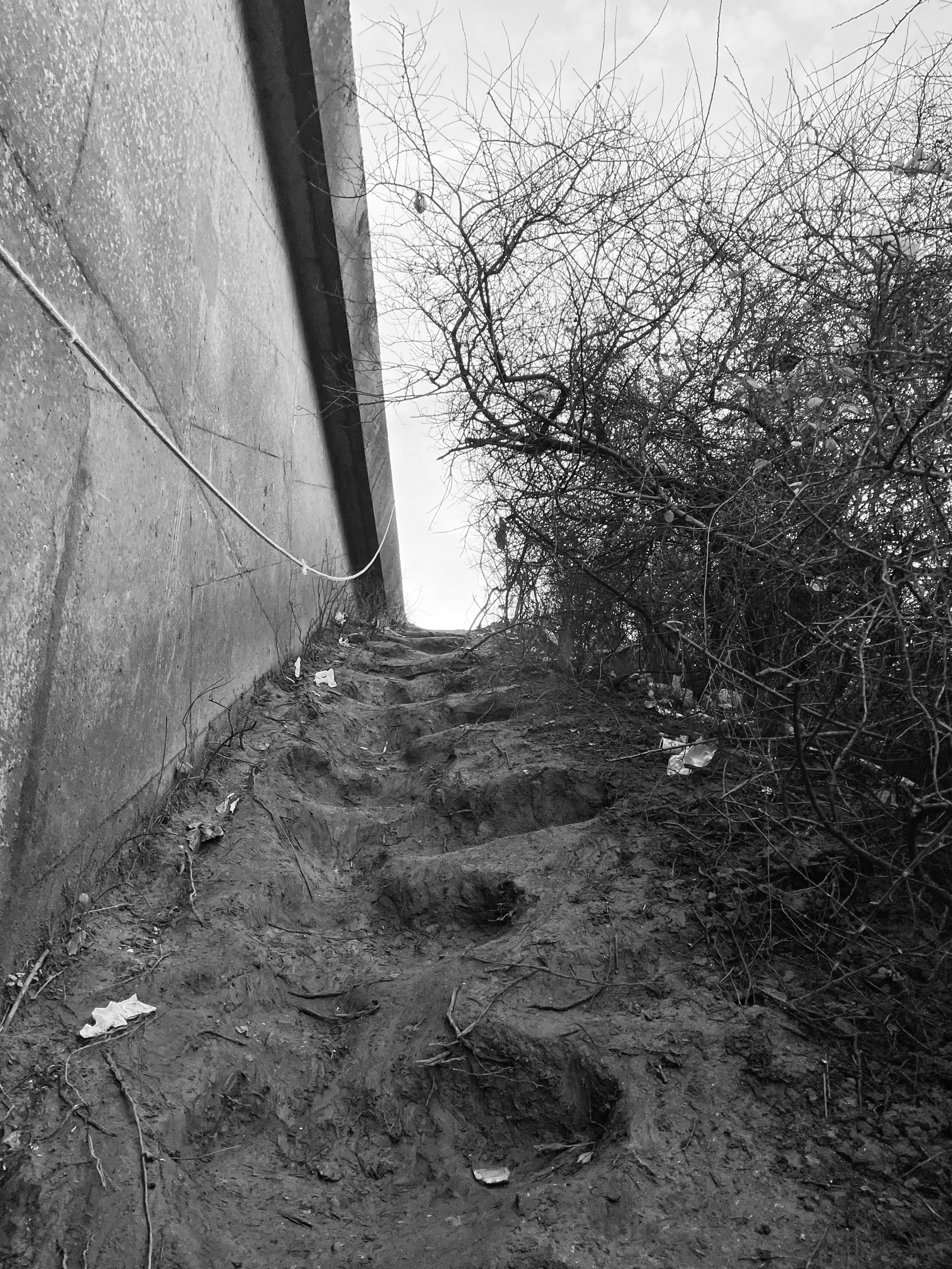 Calais, refugee camps - Black and white photo of a muddy hill, lined with concrete on one side.