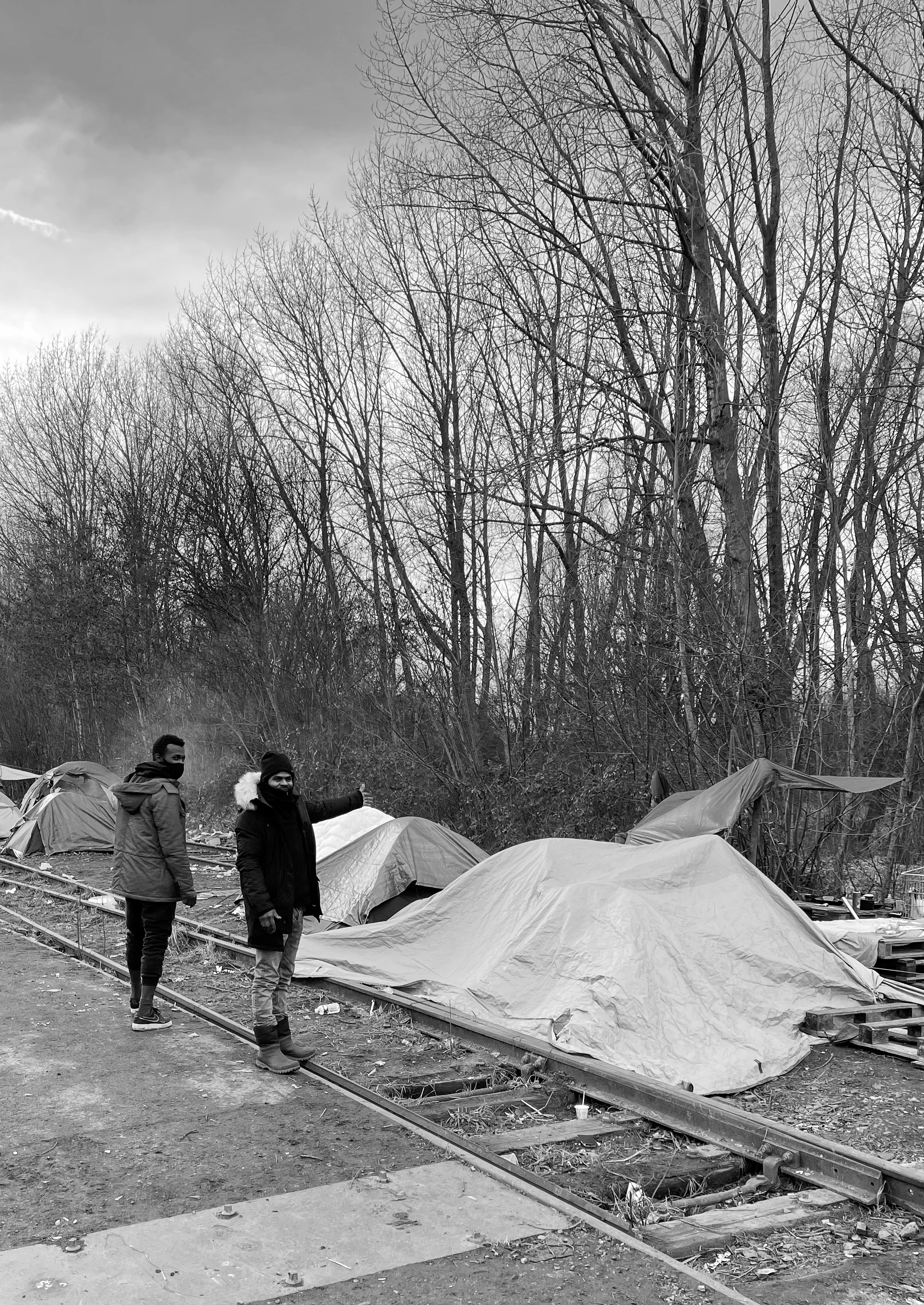 Calais, refugee camps - Black and white photo of two men in large coats stood on a disused rail track.