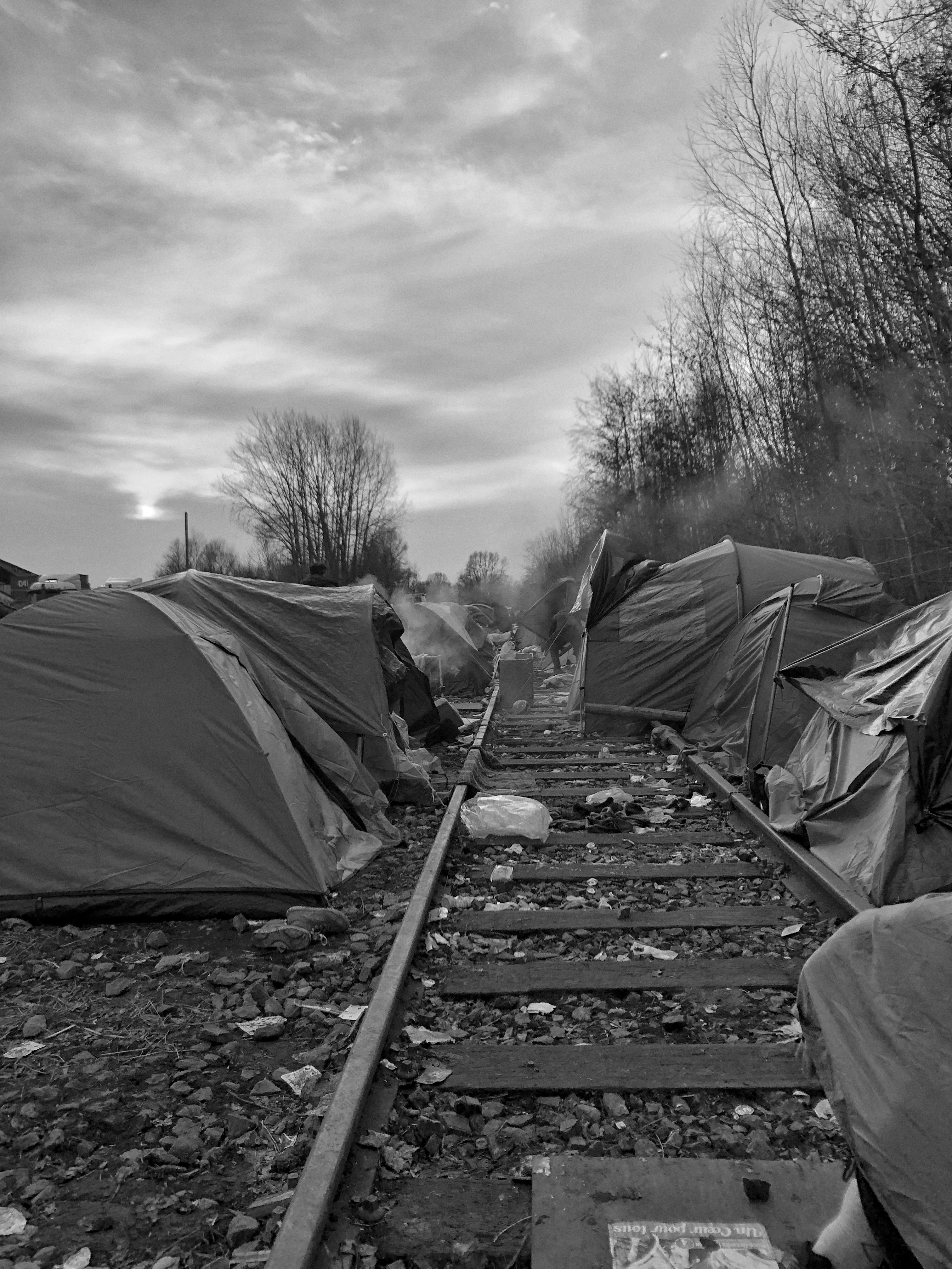 Calais, refugee camps - Black and white photo of a row of tents erected on a disused rail track.
