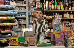A corner shop owner in front of a shelf of alcohol