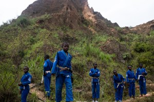 Mehrere junge Kameruner stehen in ihren blauen Jiu-Jitsu-Overalls in der Sandgrube, in der sie arbeiten; mit seiner Kampfsport-Stiftung will der berühmte MMA-Champion Francis Ngannou den Jugendlichen aus seinem Heimatland eine neue Perspektive bieten