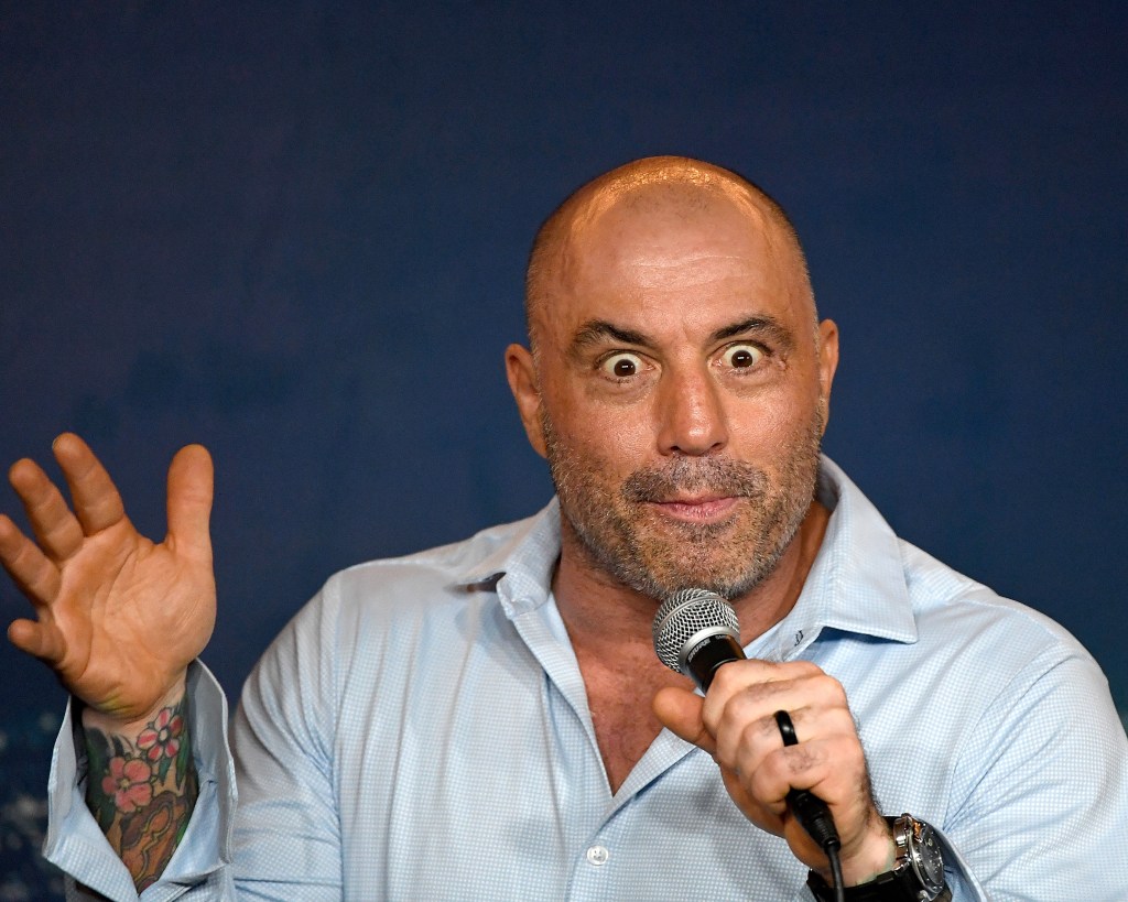 Joe Rogan appears onstage holding a mic