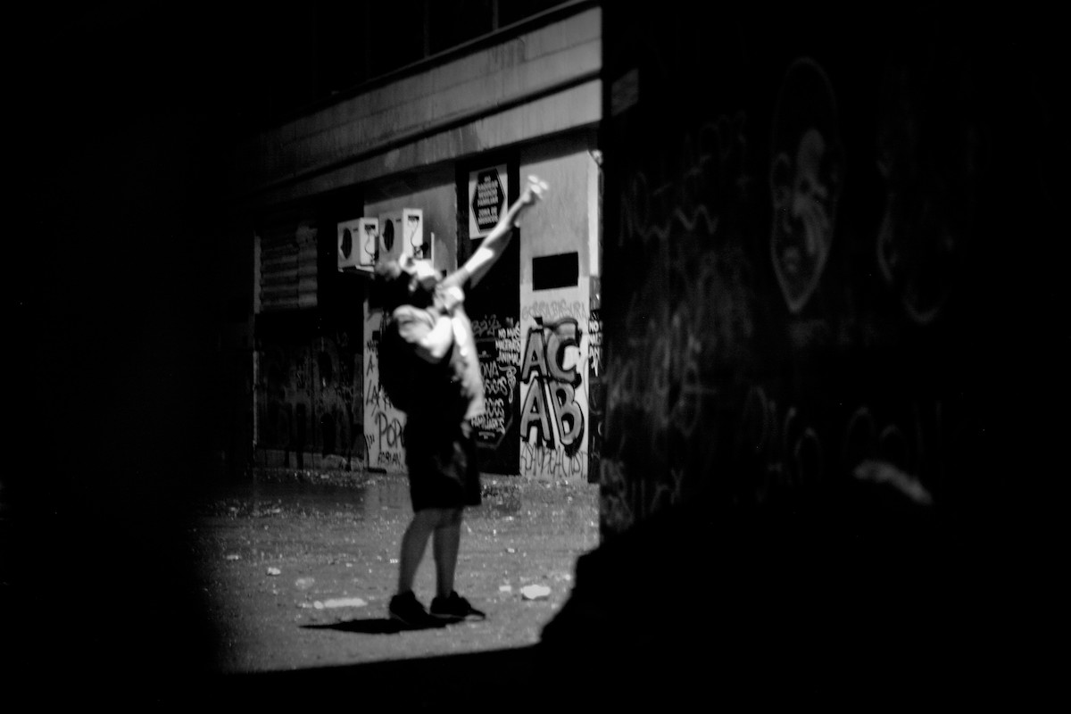 Chile protests – black and white photo of a protester with their face covered, throwing something up in the air.