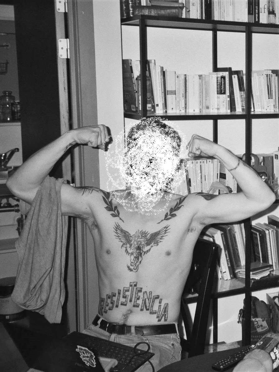 Chile protests – black and white photo of a shirtless man sitting on a chair with his laptop on his lap, showing off a tattoo reading