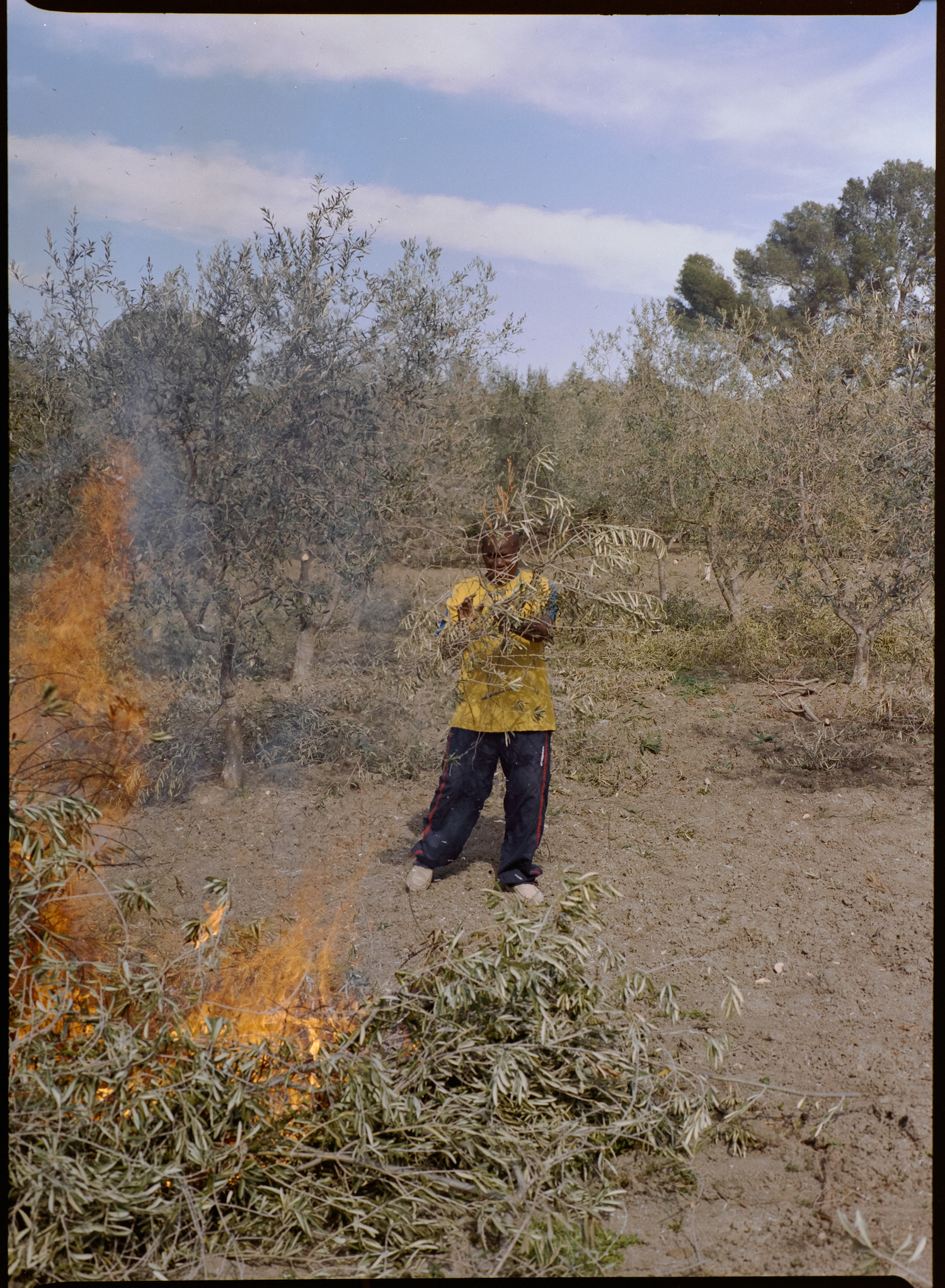 Michele Battilomo, De-population, Basilicata – Child wearing a yellow shirt and joggers burning leaves in a big fire.