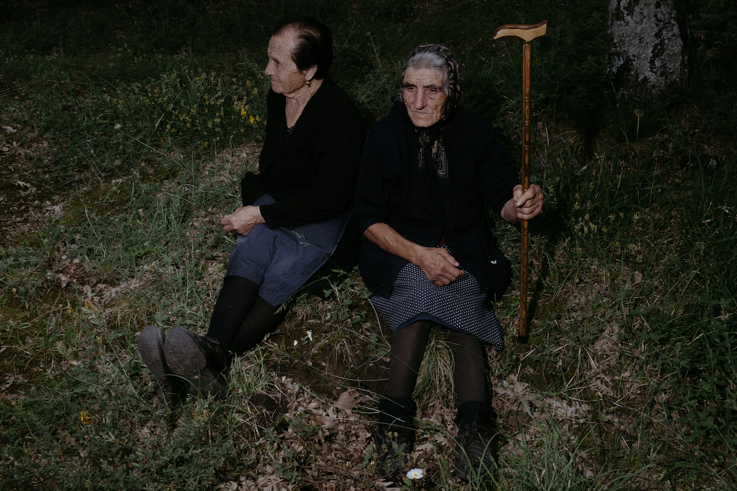 Michele Battilomo, De-population, Basilicata – two old women in dark clothing sitting side by side on a grassy field.