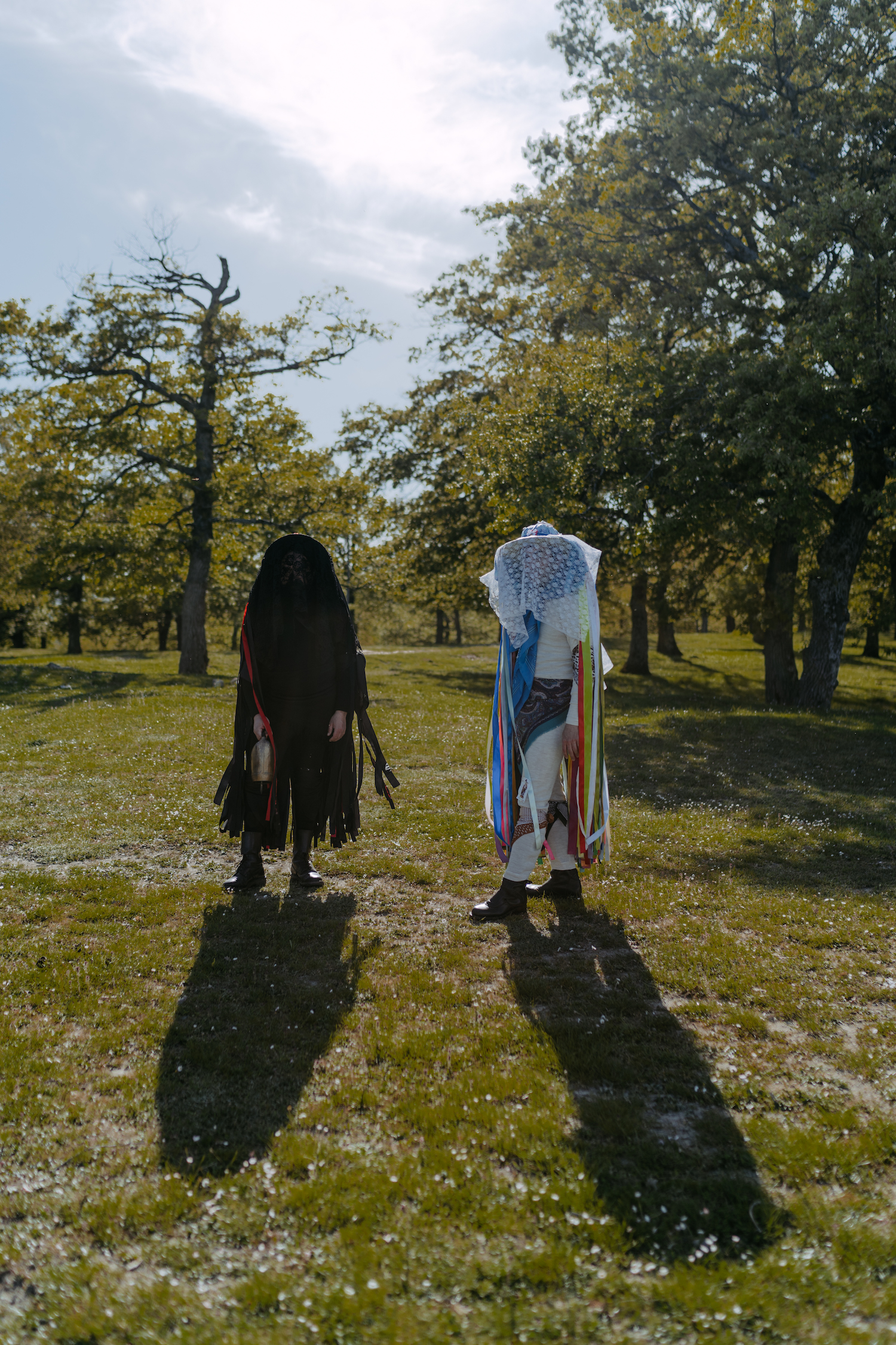 Michele Battilomo, De-population, Basilicata – Left: person in black clothing with fringe, covering their face too. Right: person in white clothing with colourful ribbons hanging from it and a veil covering their face.