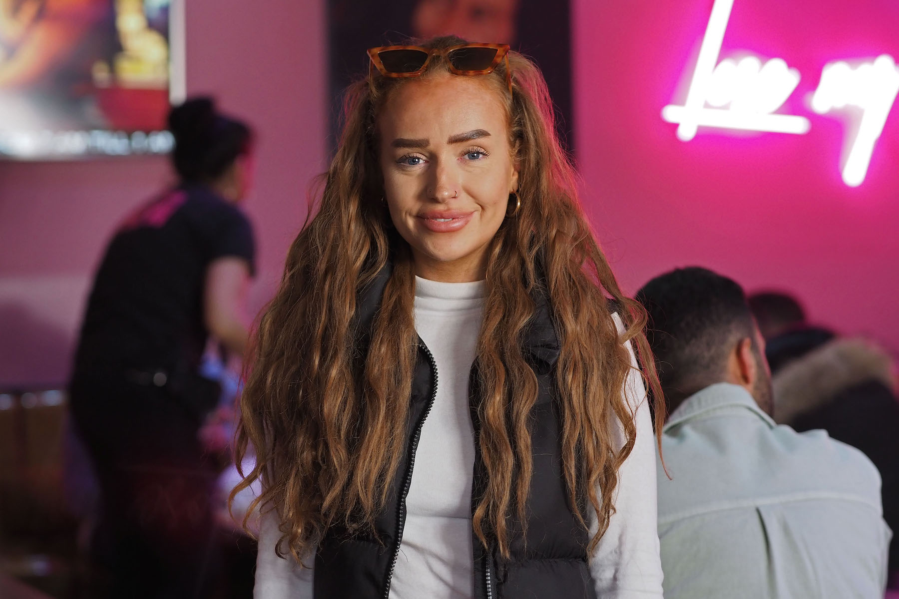 Eine junge Frau mit langen blonden Haaren und hochgeschobener Sonnenbrille in einem Raum mit violetten Wänden
