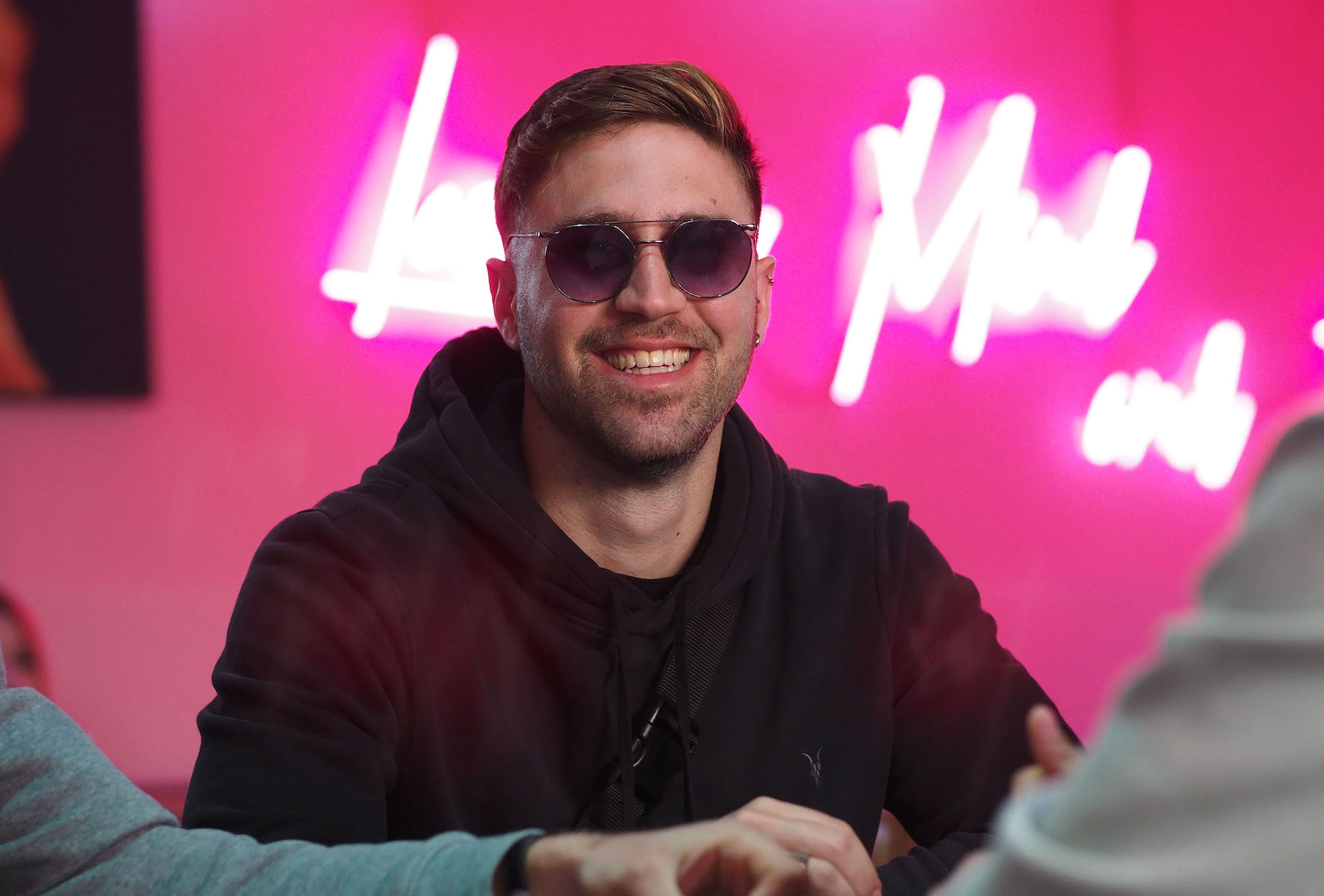 Ein grinsender junger Mann mit großer Sonnenbrille vor einem violetten Hintergrund