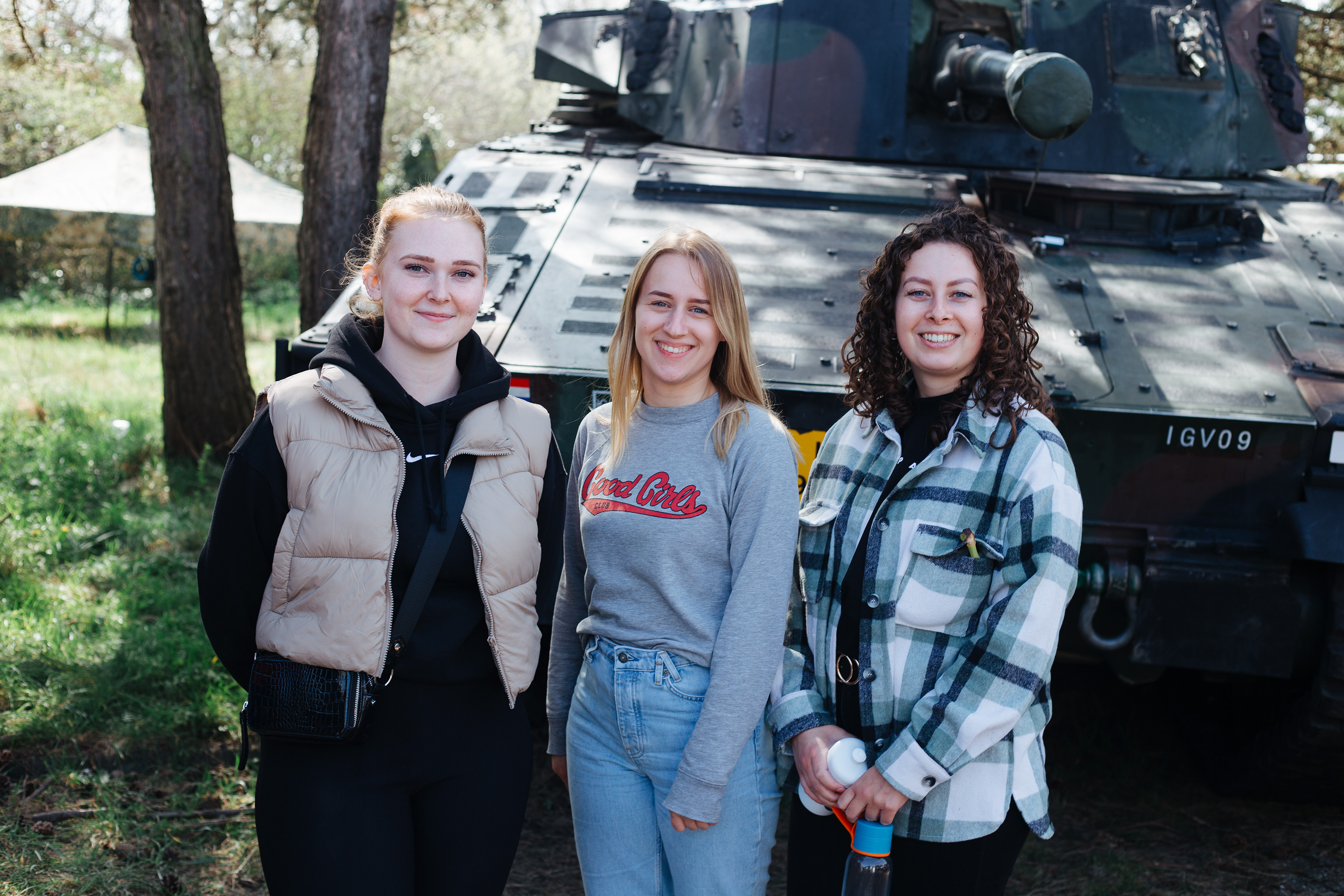 Army recruitment, Fort 1881 – three young women posing in casual clothes in front of a tank.
