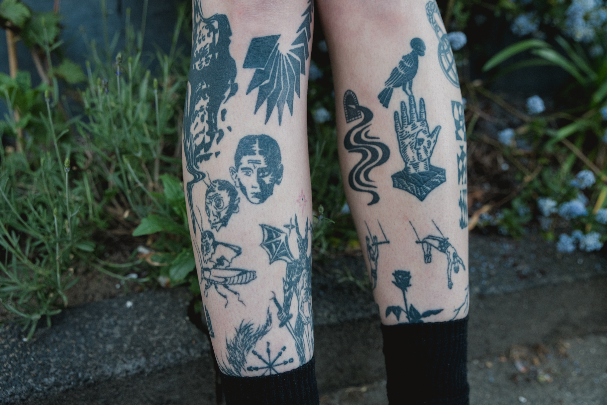 Polina Frank – photo of legs under the knee. They're covered in black and white tattoos of different surrealist subjects.