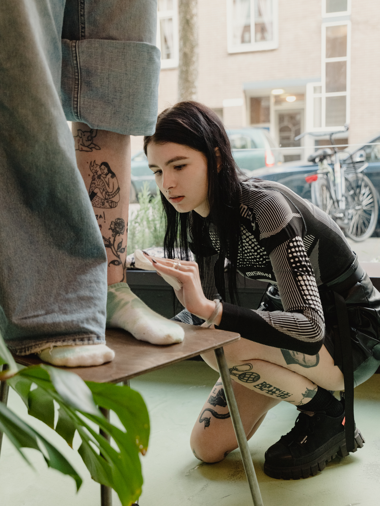 Polina Frank – young woman in all black disinfecting a tattoo on someone's lower leg.
