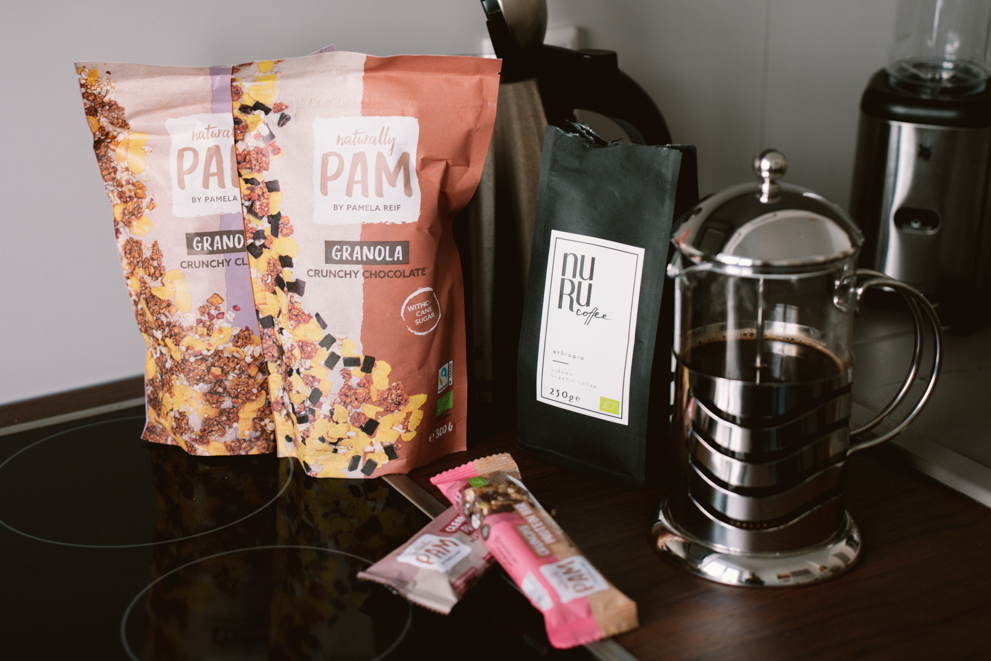 Auf einer Arbeitsfläche stehen zwei Packungen Müsli, zwei Müsliriegel von Pamela Reif und Kaffee von Sara Nuru.