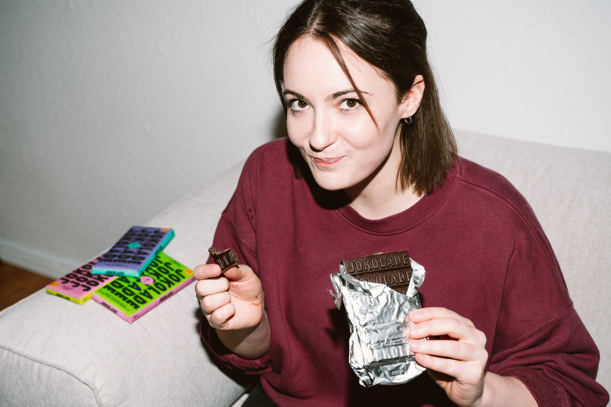 Die Autorin probiert eine Sorte von Joko Winterscheidts Jokolade. Auf dem Sofa neben ihr liegen weitere Sorten.
