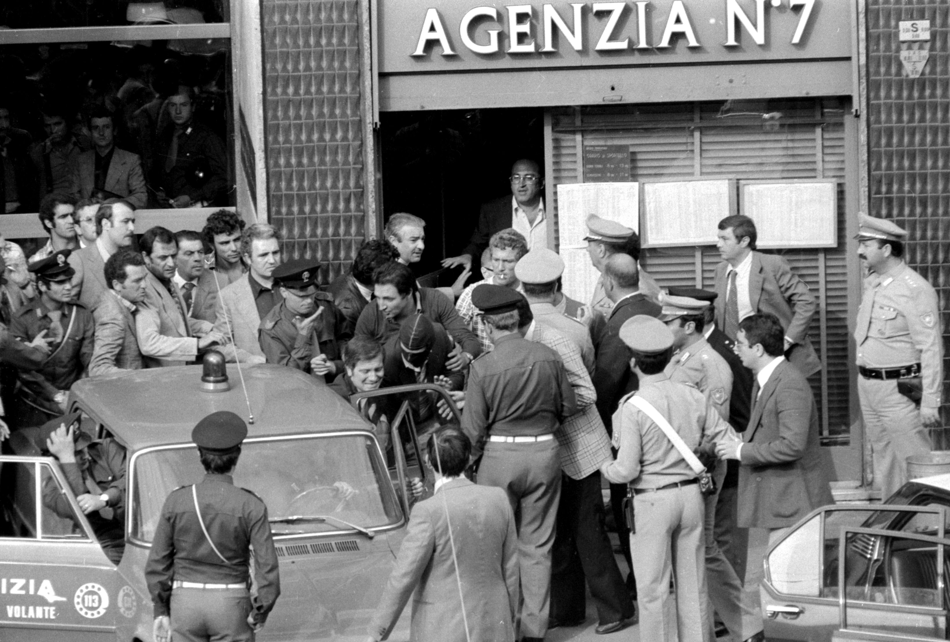 Schwarzweißfoto von einer Menschenmenge vor einem Gebäude um eine Polizeiwagen