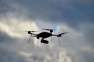 The silhouette of an aerial drone flying against a cloudy sky.