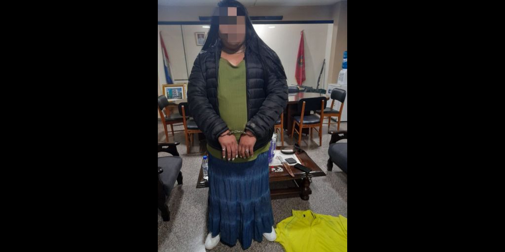 Lelaki gemuk mengenakan kaus hijau, rok biru panjang dan jaket hitam. Tangan diborgol
