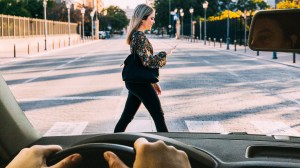 Durch die Windschutzscheibe blicken wir auf eine Frau, die über die Straße geht, wo Frauen oft Catcalling erleben.