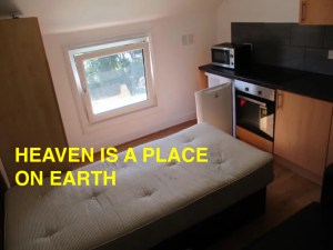 A single bed next to fridge, oven and wardobe.
