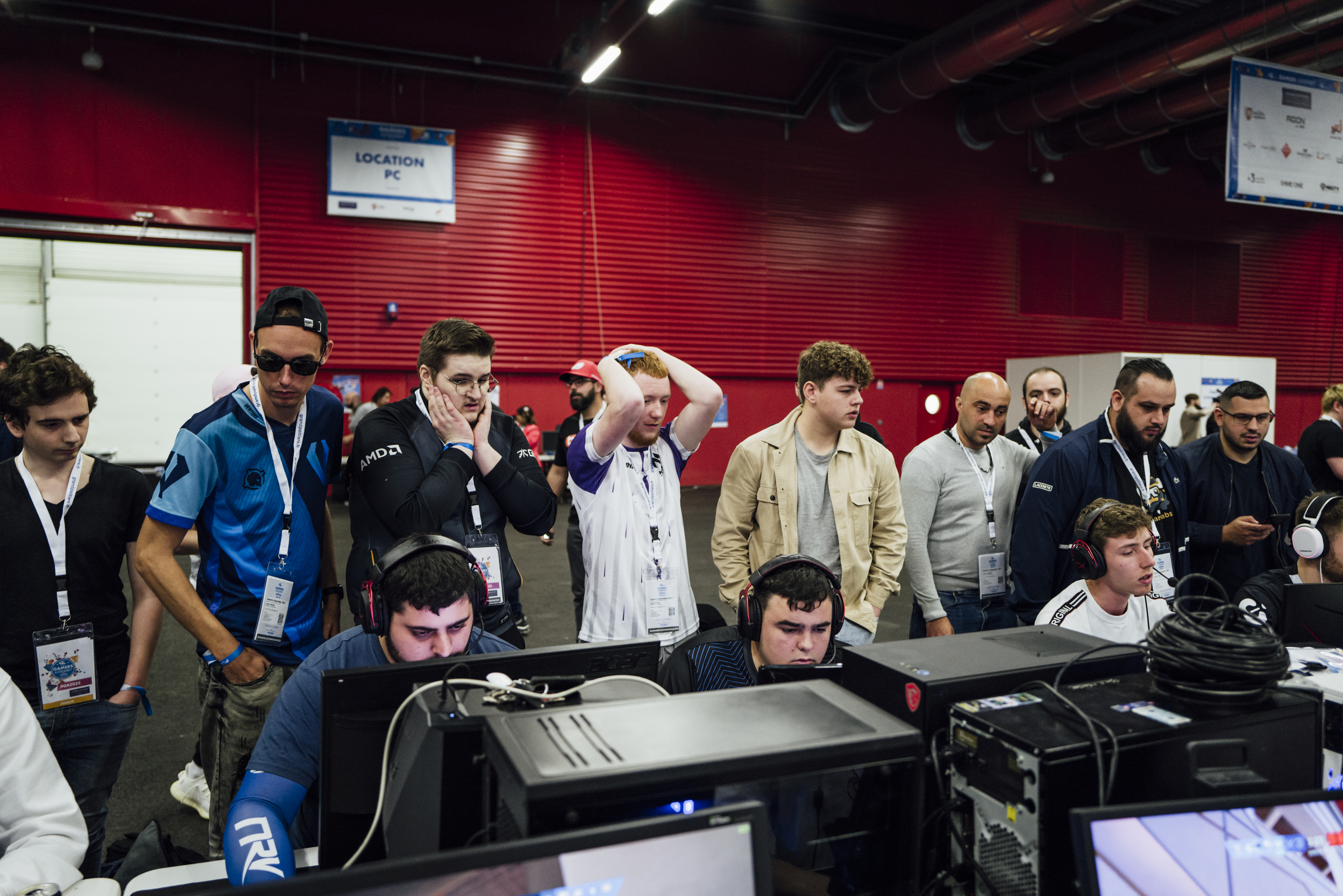 Gamers Assembly, LAN party – group of guys standing behind their teammates who are playing, looking sad and worried because of their performance.