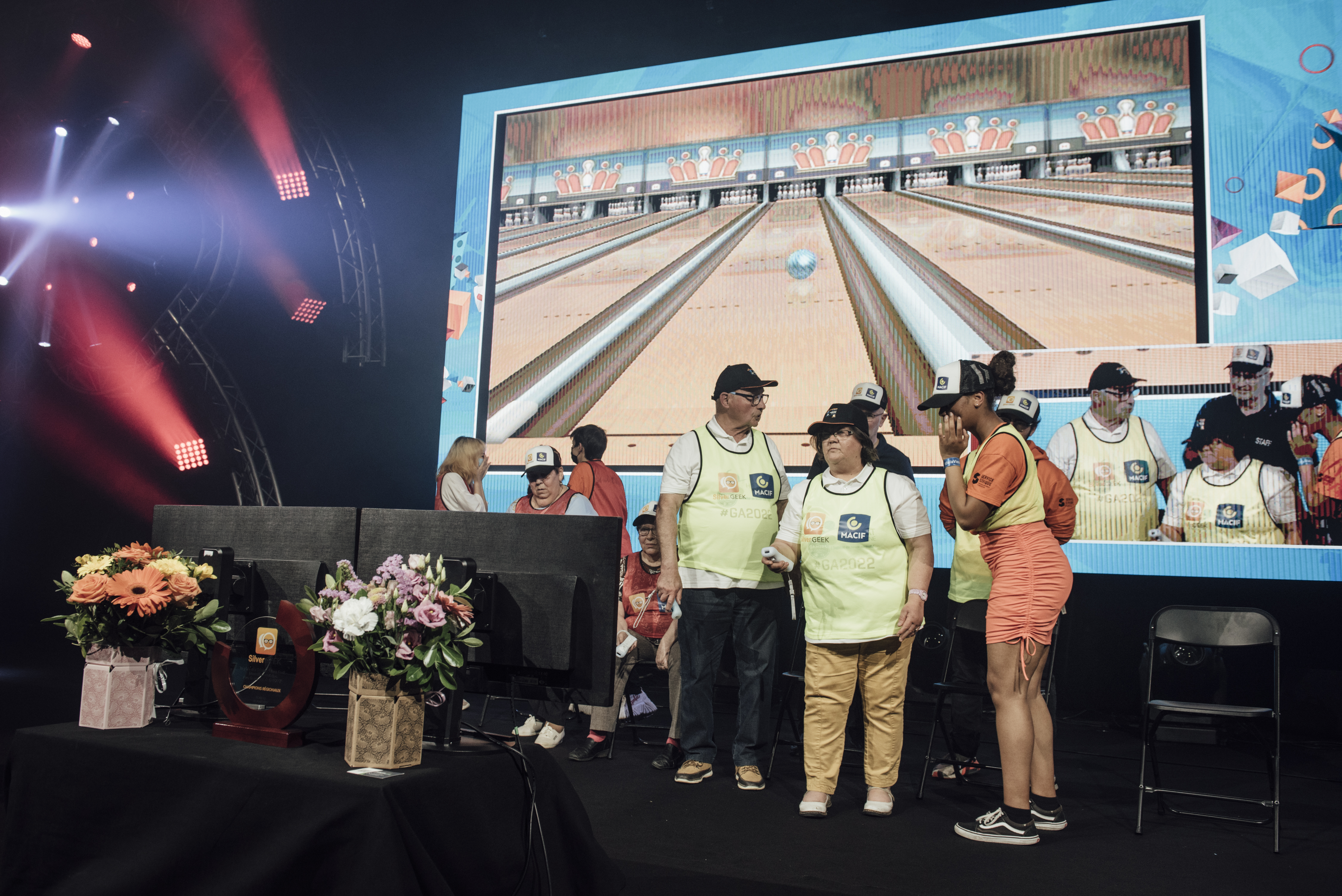 Gamers Assembly, LAN party – group of elderly people on a stage, holding wii controllers in front of large screens. On the background, a widescreen is showing the game to the public.