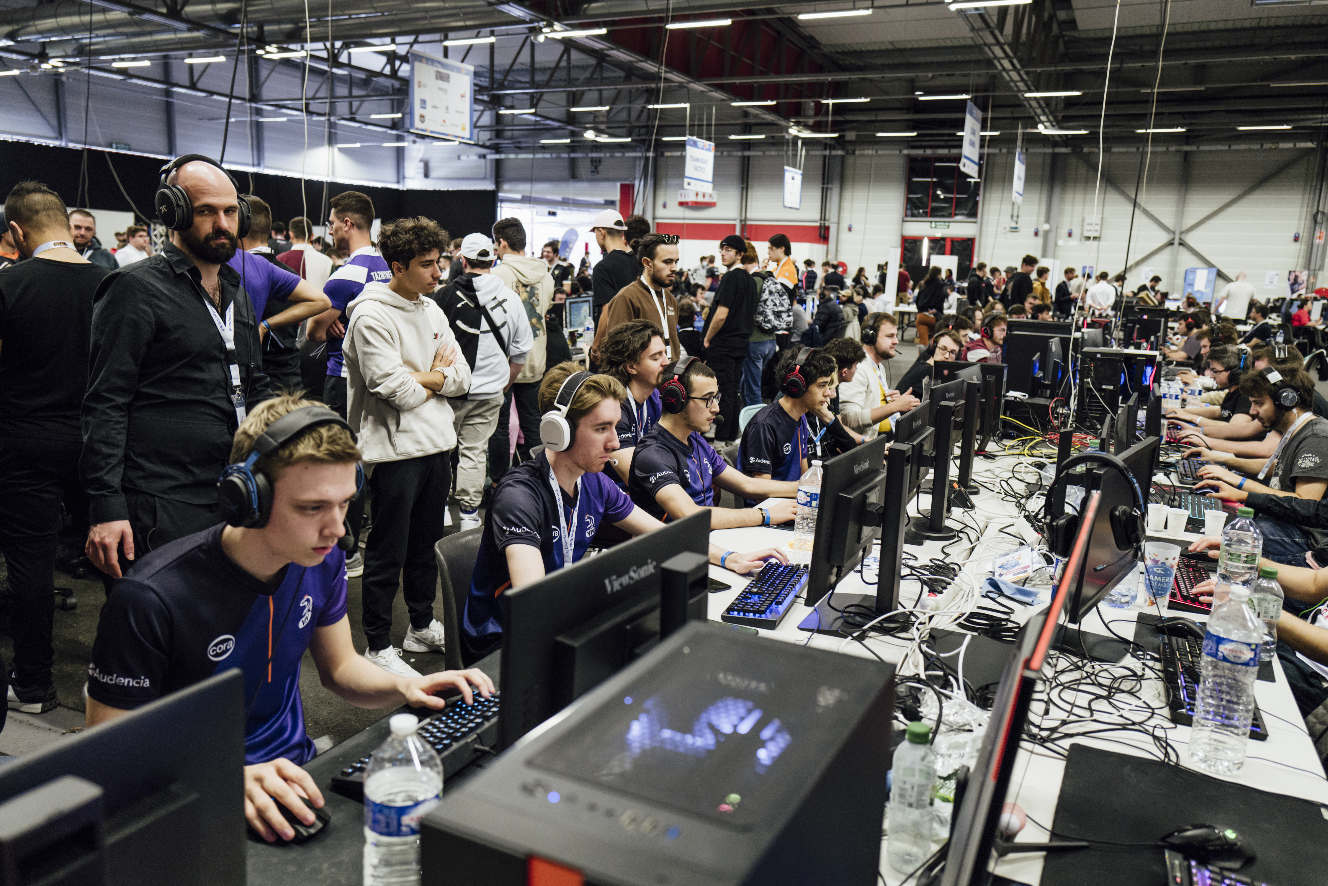 Gamers Assembly, LAN party – Rows of gamers playing as their teammates watch behind them and cheer them on.
