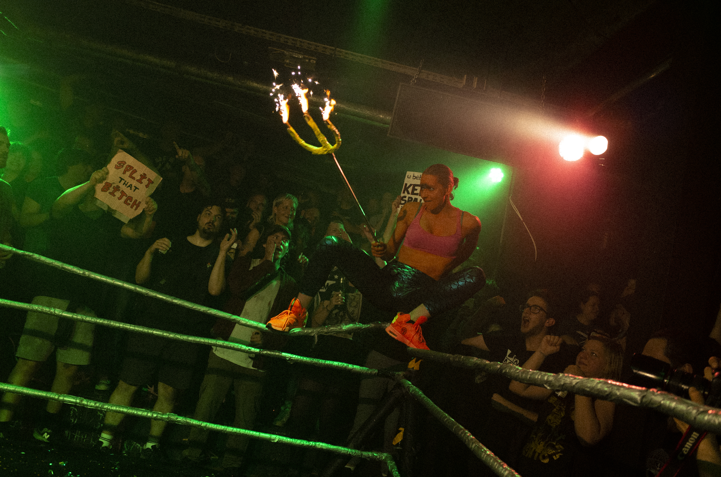 Rock & Wrestling, Hamburg – Woman wearing a pink crop top, mermaid leggins and orange sneakers, holding a trident on fire and getting ready to jump from the corner of the ring