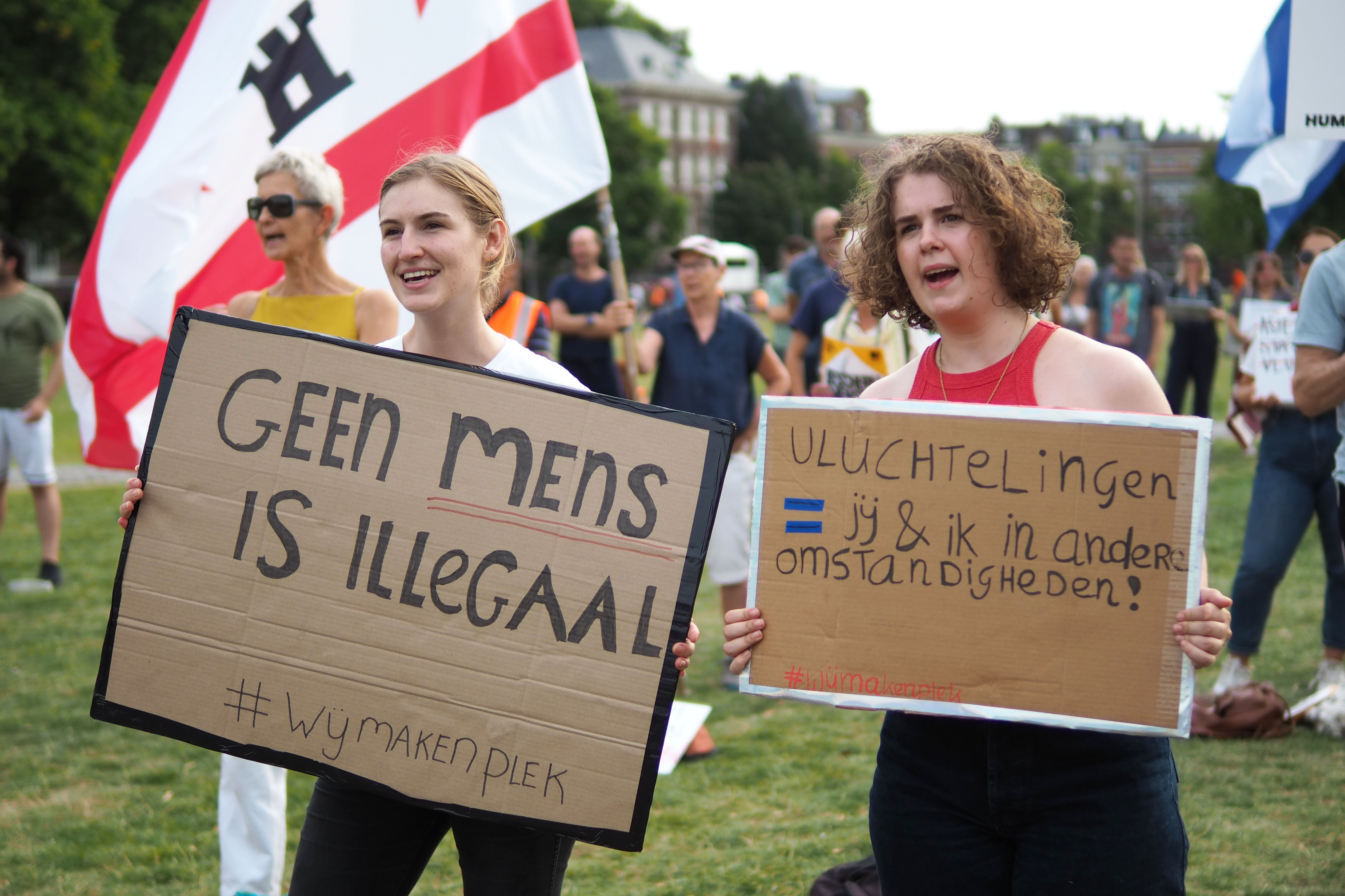 Netherlands refugee crisis, Ter Appel, protest – two young women holding signs in front of a scattered crowd on a meadow