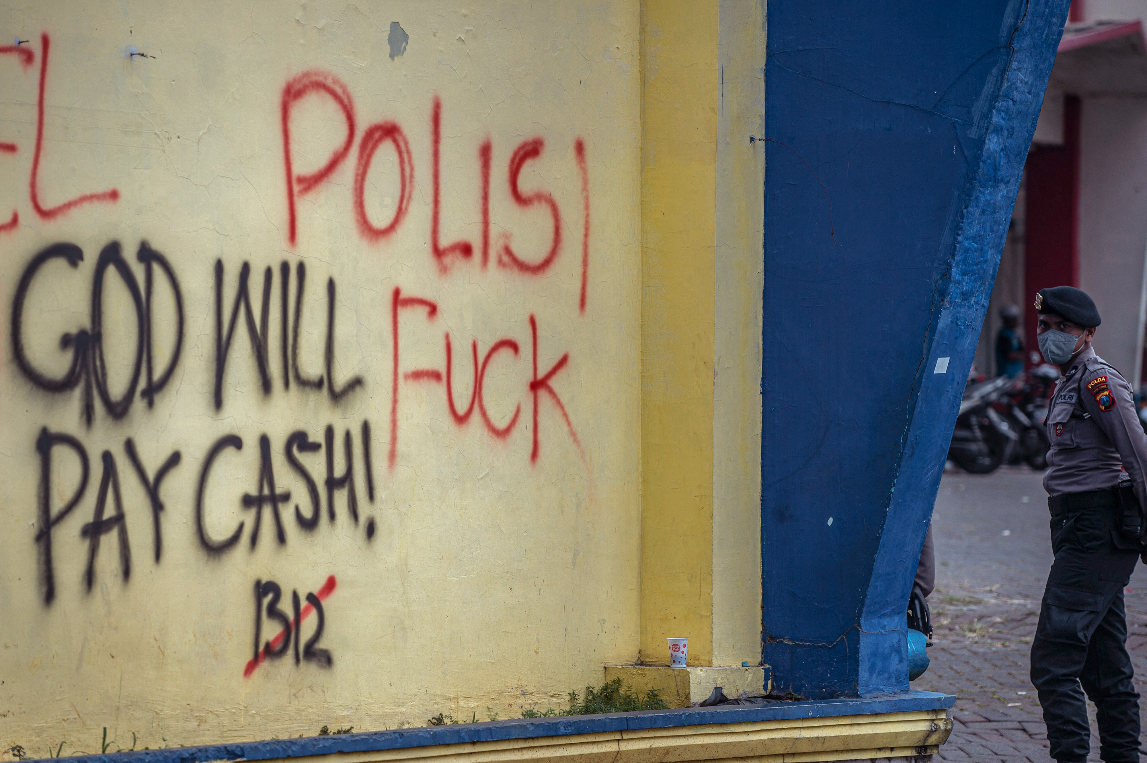 Anggota polisi berdiri di depan tembok Stadion Kanjuruhan Malang yang bertuliskan “Polisi F**k”. Foto: Juni Kriswanto / AFP