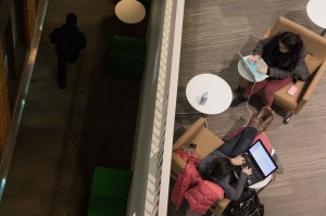 An overhead shot of students sitting in chairs using laptops in a library.