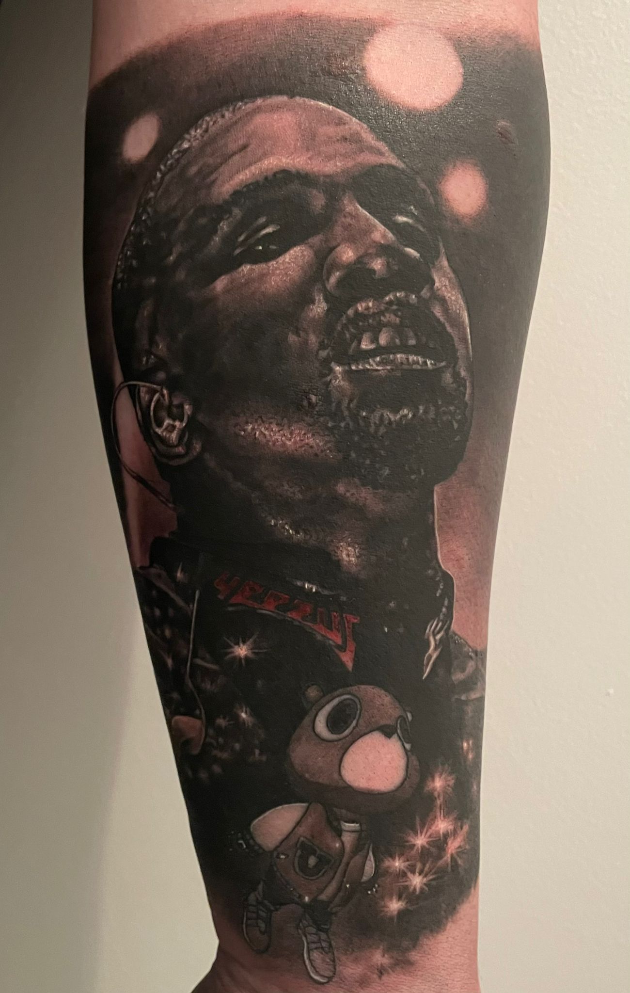 Leg tattoo of Kanye West's face as a tattoo next to Graduation bear