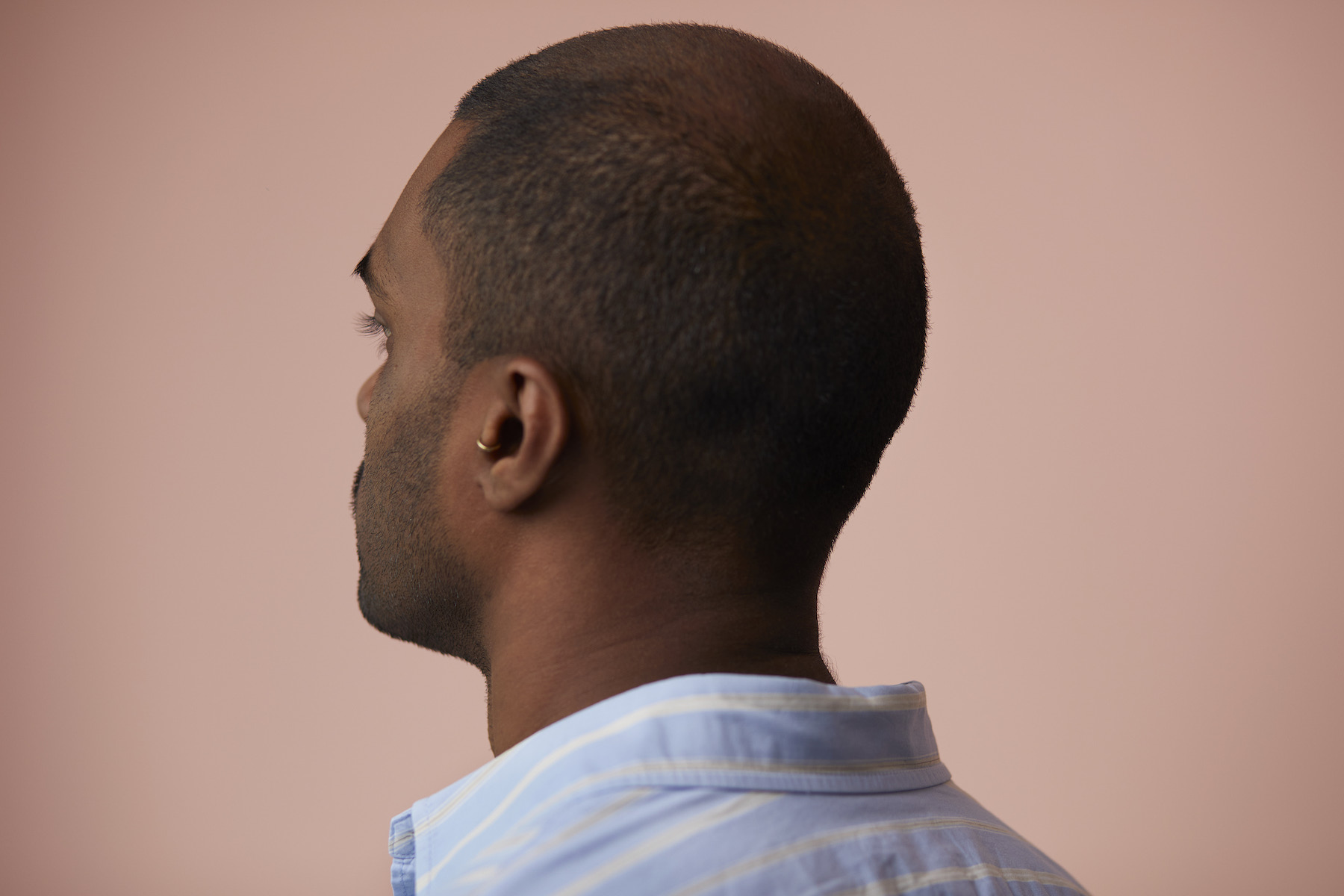 Picture of a man with short black hair and a balding spot on top, taken from behind his back.