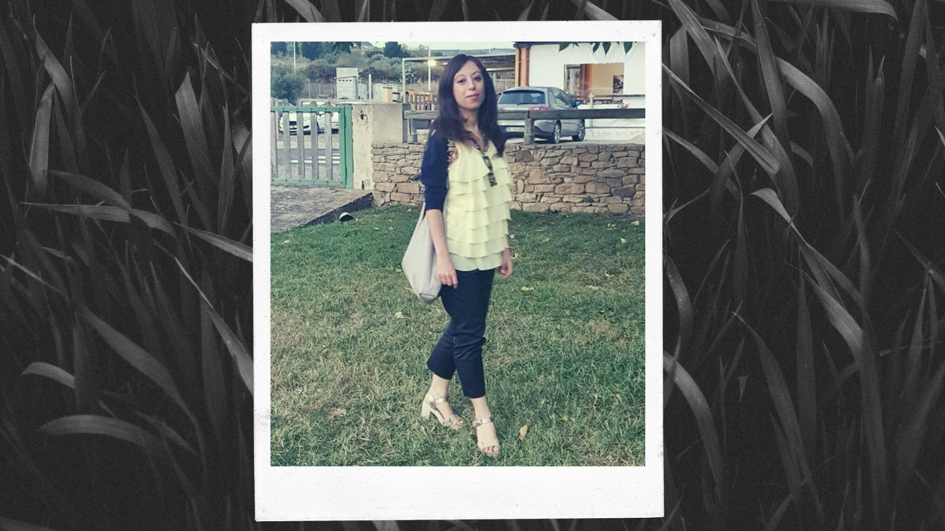 Alessandra,Unione Satanisti Italiani – woman with long dark hair wearing a white, teared top with a black cardigan, black pants, a big beige tote and golden heeled sandals and posing in the grass in front of a house