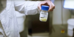 Ein Chemiker hält ein Glas hoch mit der Pro-Drug 1V LSD